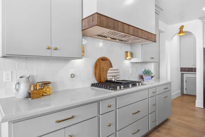 Kitchen featuring arched walkways, backsplash, light wood finished floors, stainless steel gas cooktop, and gray cabinets