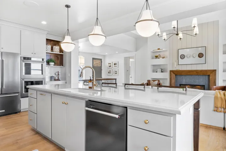 Kitchen with a fireplace, stainless steel appliances, white cabinets, open shelves, and an island with sink