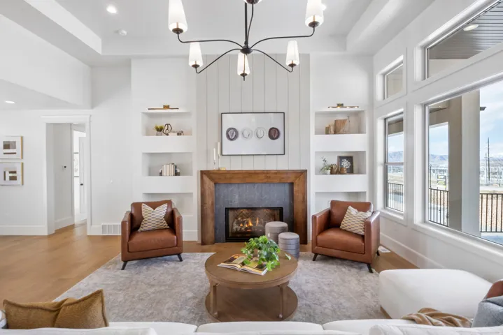 Living area featuring built in features, hanging lights, wood finished floors, a lit fireplace, and a high tray ceiling
