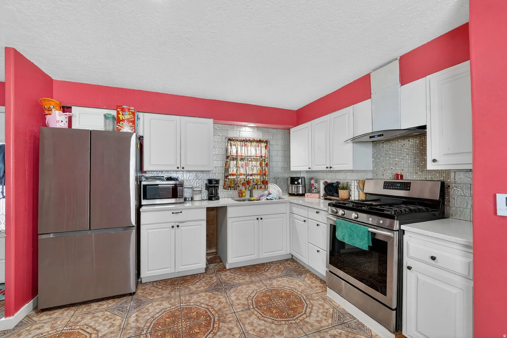 Kitchen featuring stainless steel appliances, white cabinetry, a textured ceiling, backsplash, and light tile patterned floors