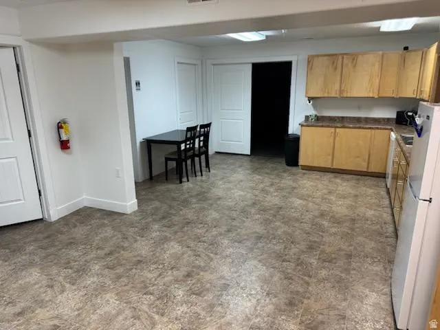 Kitchen with dark countertops, freestanding refrigerator, and light wood finish cabinetry