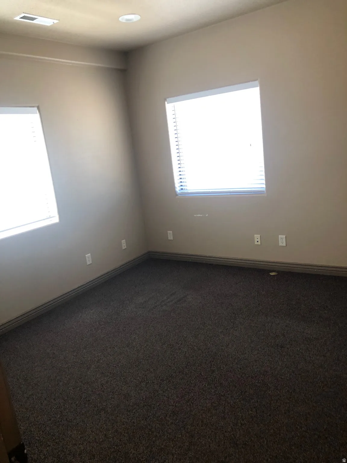 Empty room featuring dark colored carpet and plenty of natural light