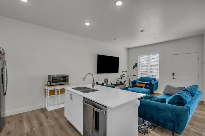 Kitchen with open floor plan, white cabinets, a kitchen island with sink, light wood-style flooring, and stainless steel appliances