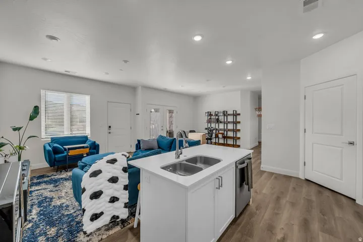 Kitchen featuring white cabinetry, an island with sink, open floor plan, wood finished floors, and recessed lighting