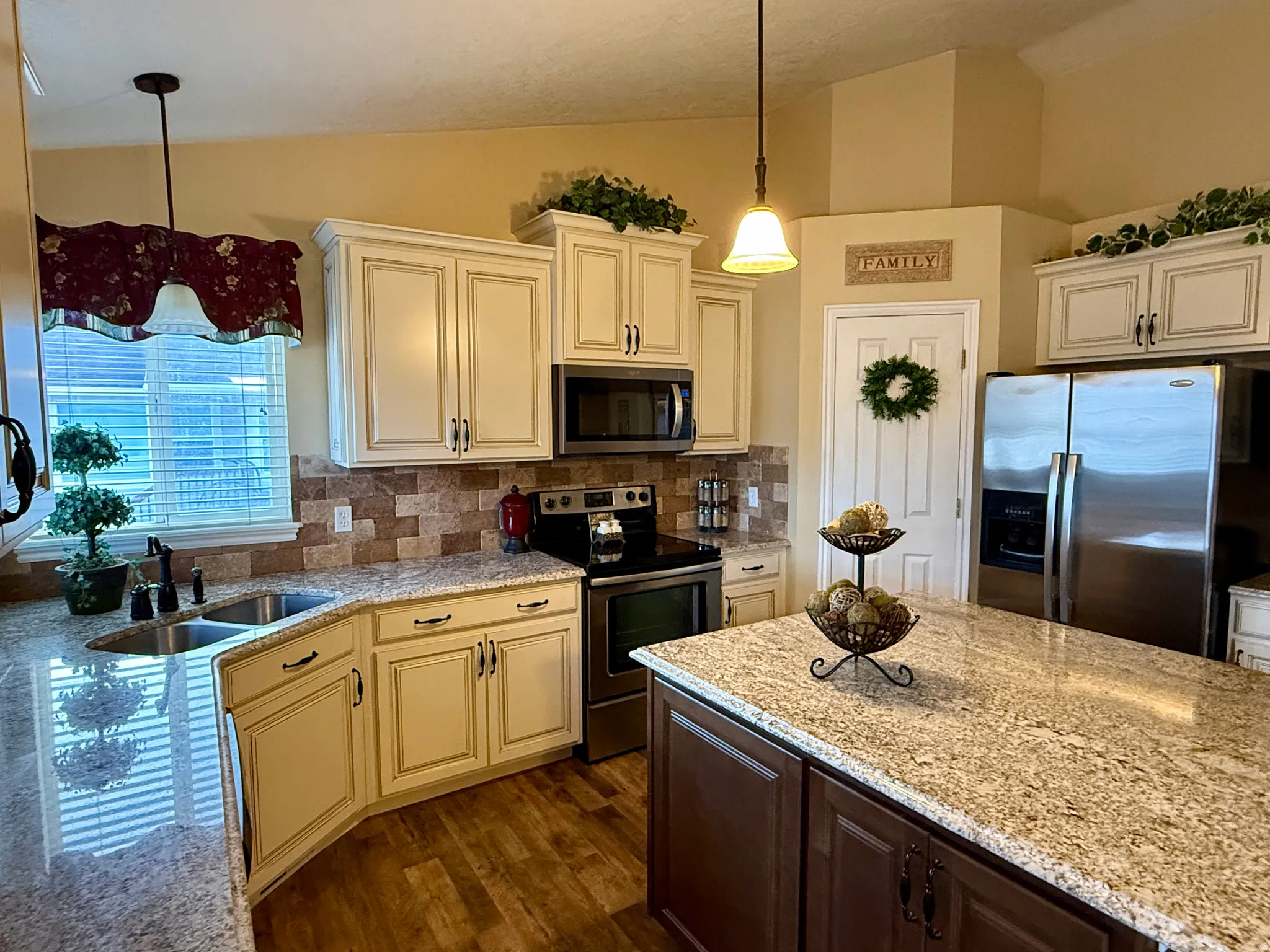 Kitchen featuring stainless steel appliances, dual tone cabinets, lofted ceiling, light stone counters, and hanging light fixtures