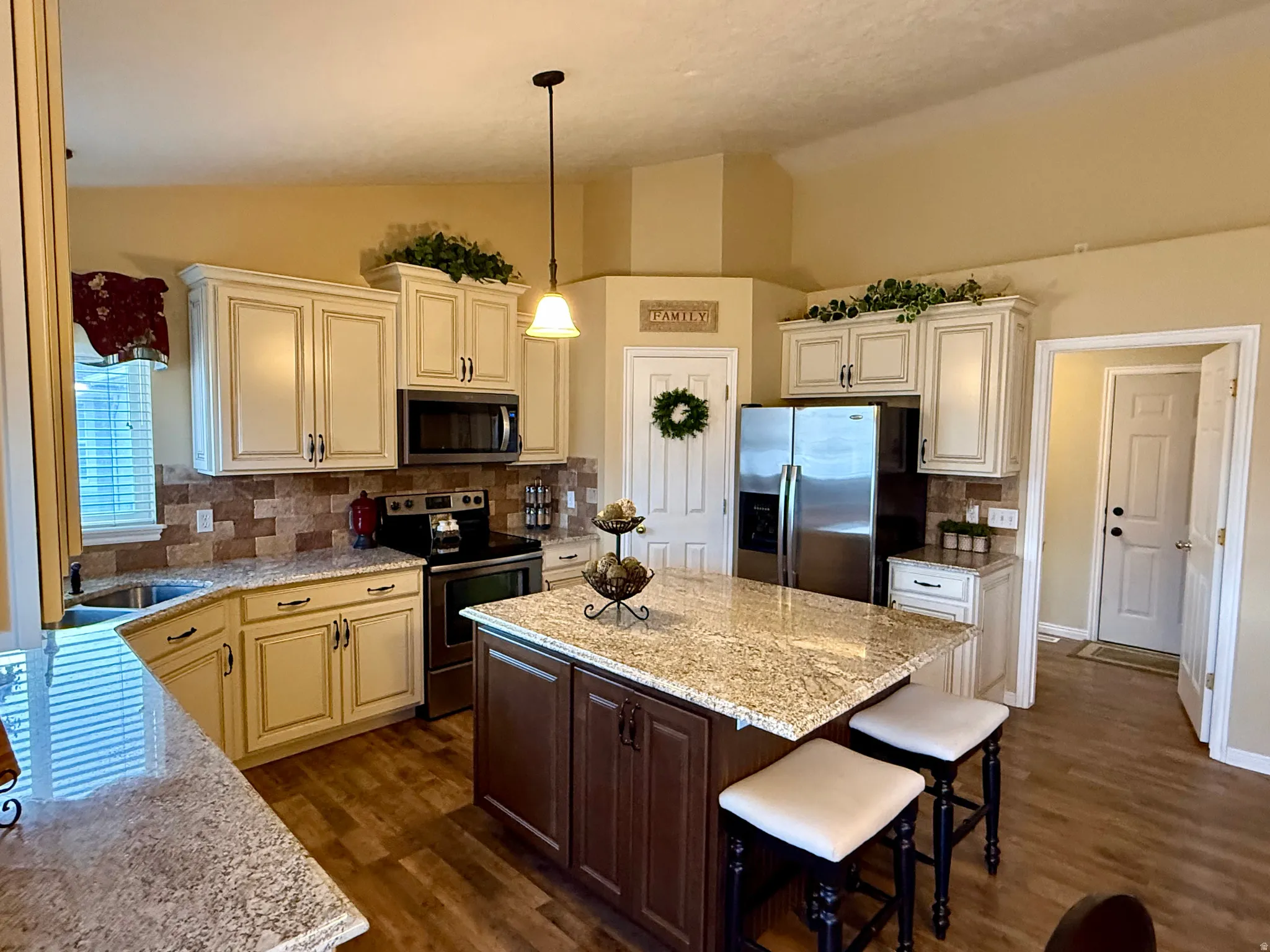 Kitchen with stainless steel appliances, light stone counters, backsplash, dark wood finished floors, and dual tone cabinets