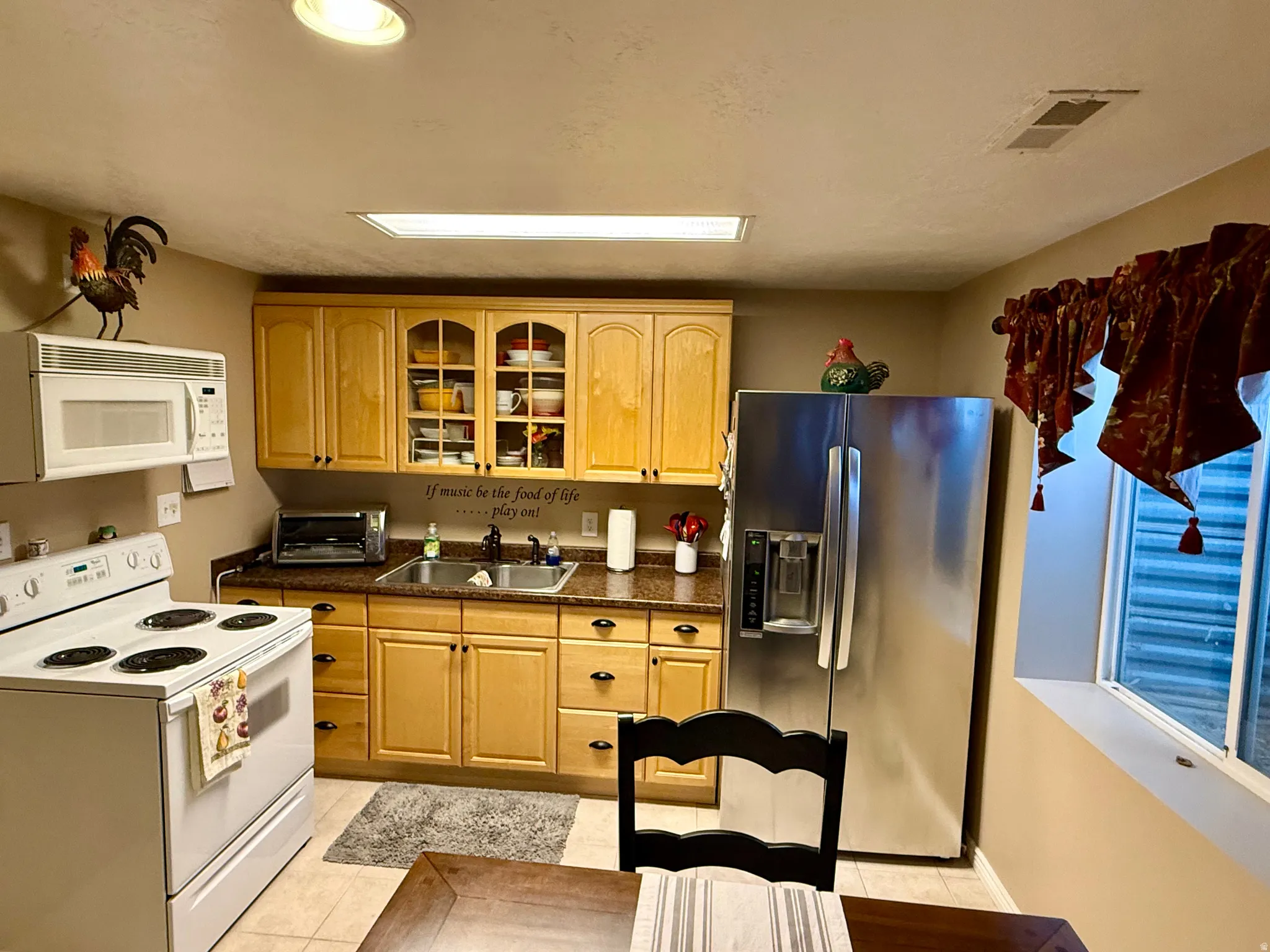Kitchen featuring white appliances, glass insert cabinets, dark countertops, and light tile patterned floors