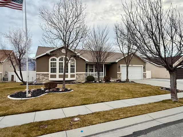 Ranch-style home featuring stucco siding, driveway, an attached garage, stone siding, and a front yard