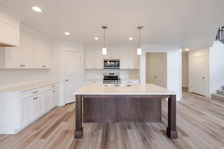 Spacious kitchen featuring an expansive center island with pendant lighting, white cabinetry, integrated stainless steel appliances, and wood-finish flooring