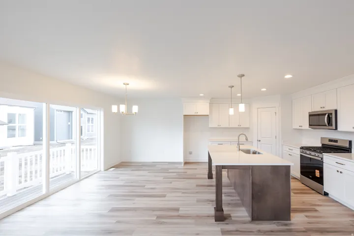 Open-concept kitchen and dining area featuring a large center island with integrated sink, stainless steel appliances, white cabinetry, and wood-finish flooring
