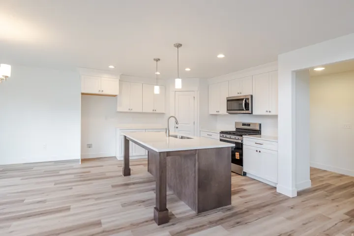Kitchen featuring a central island with a contrasting base, white shaker cabinetry, stainless steel appliances, and light-toned wood-finish flooring