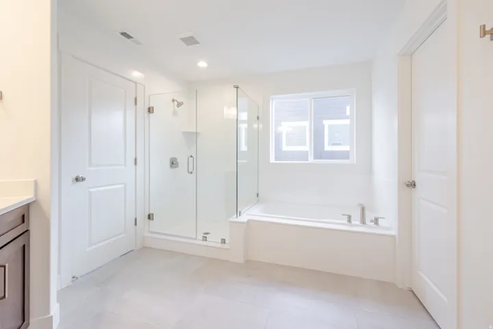 Spacious bathroom featuring a built-in soaking tub, a glass-enclosed shower, neutral tile flooring, a window, and recessed lighting