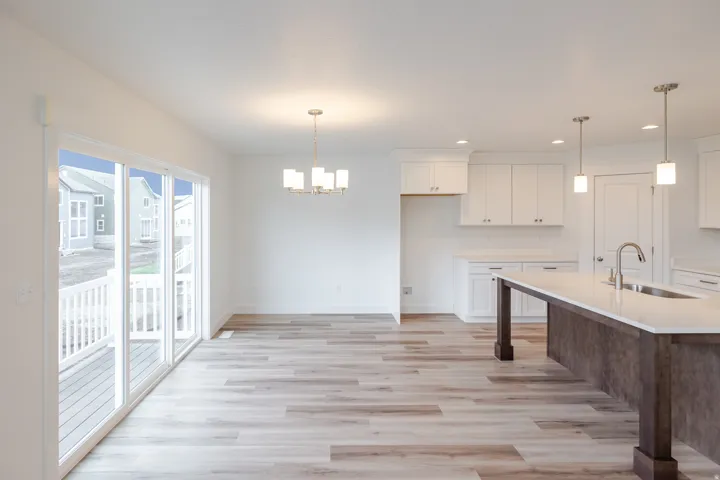 Open-concept living area featuring wood-finish flooring, white cabinetry, a kitchen island with an undermount sink, and sliding glass doors to a deck