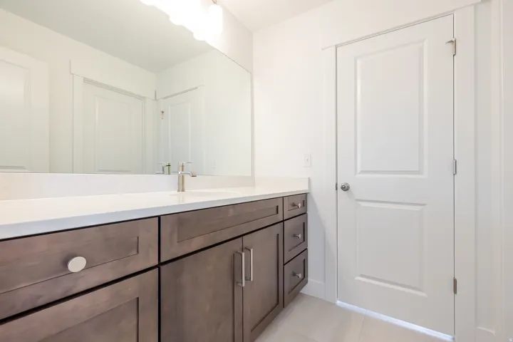 Vanity featuring dark wood cabinetry with brushed nickel hardware, a white countertop, and a rectangular undermount sink