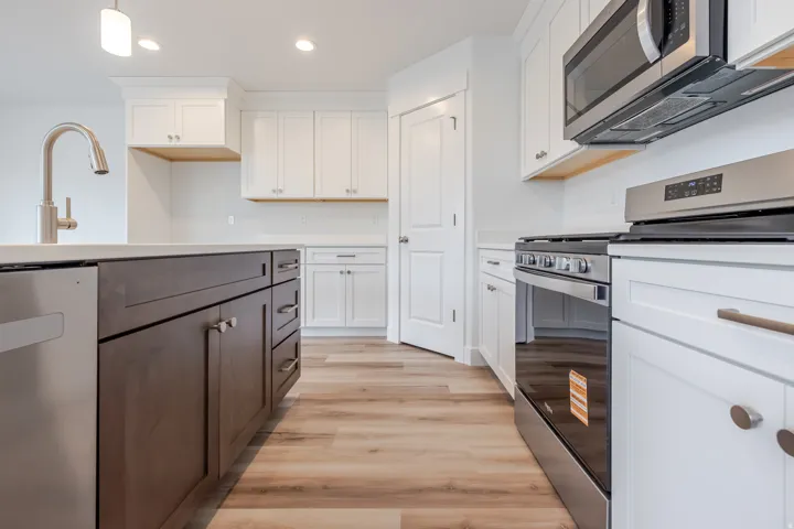 Modern kitchen featuring wood-finish flooring, white perimeter cabinetry, and a dark-toned island with integrated stainless steel appliances