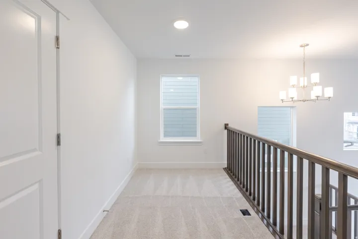 Upper-level hallway featuring neutral carpeting, white walls, and a multi-pane window