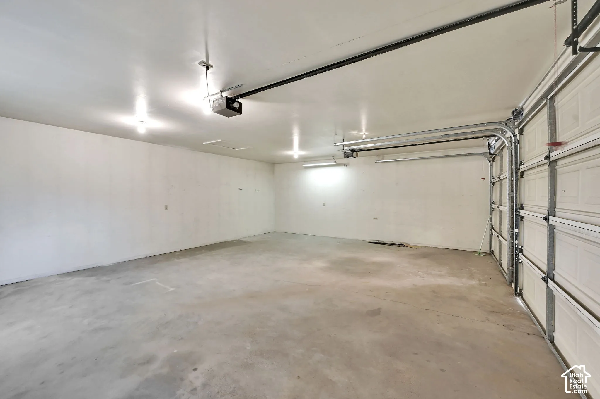 Spacious 3 car garage featuring a concrete floor, white interior walls, overhead lighting, and an automatic garage door opener.