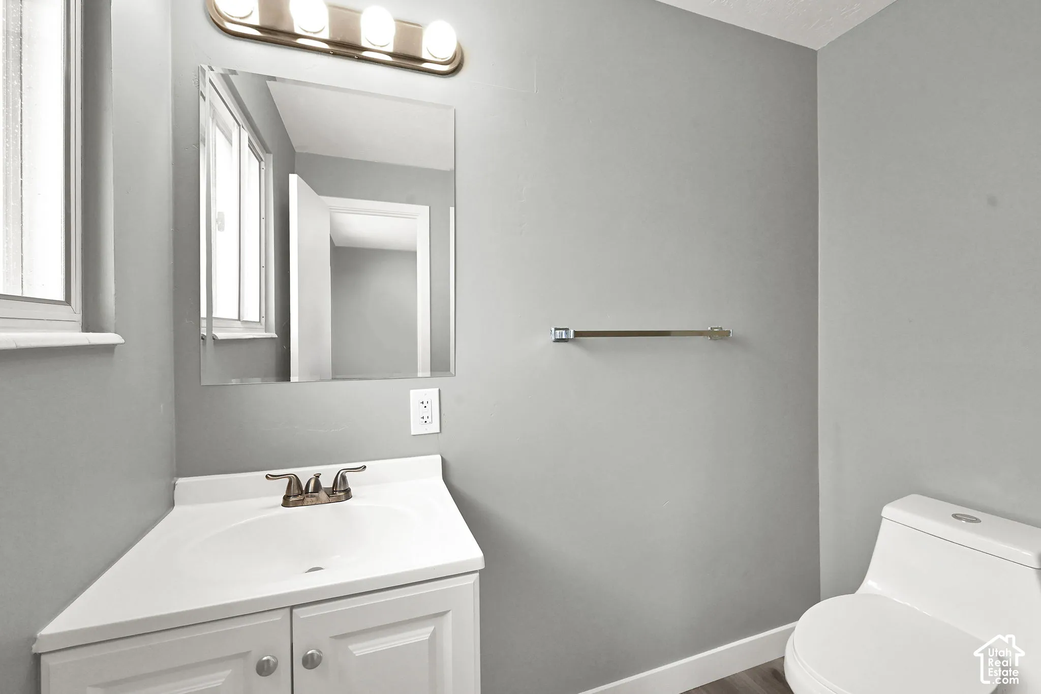 White corner vanity with an integrated sink, brushed brass faucet, and a rectangular mirror.