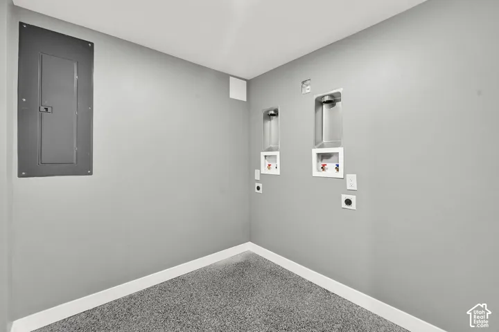 Dedicated laundry area featuring a durable epoxy-coated concrete floor, white baseboards, and pre-installed hookups for two stackable washer and dryers.