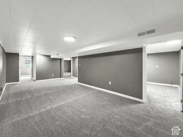 Expansive carpeted area with neutral gray walls, white trim, recessed lighting, and a drop ceiling