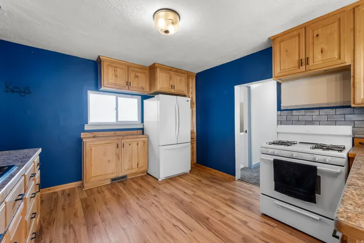 Kitchen with white appliances, light wood-style flooring, backsplash, and a textured ceiling