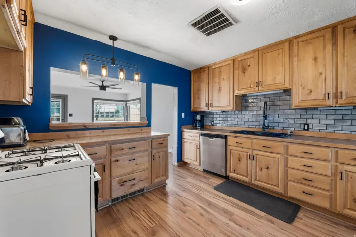 Kitchen featuring pendant lighting, stainless steel dishwasher, light wood-type flooring, white range with gas stovetop, and light countertops