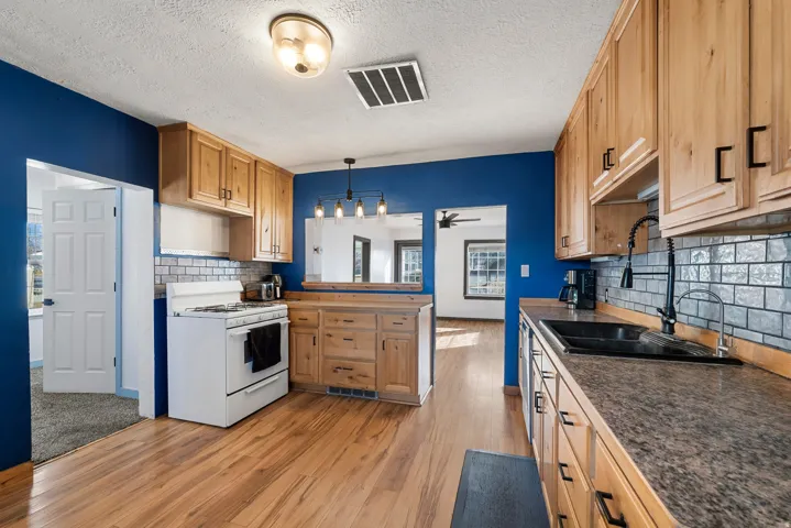 Kitchen with white gas range oven, light wood-type flooring, a peninsula, dark countertops, and a textured ceiling