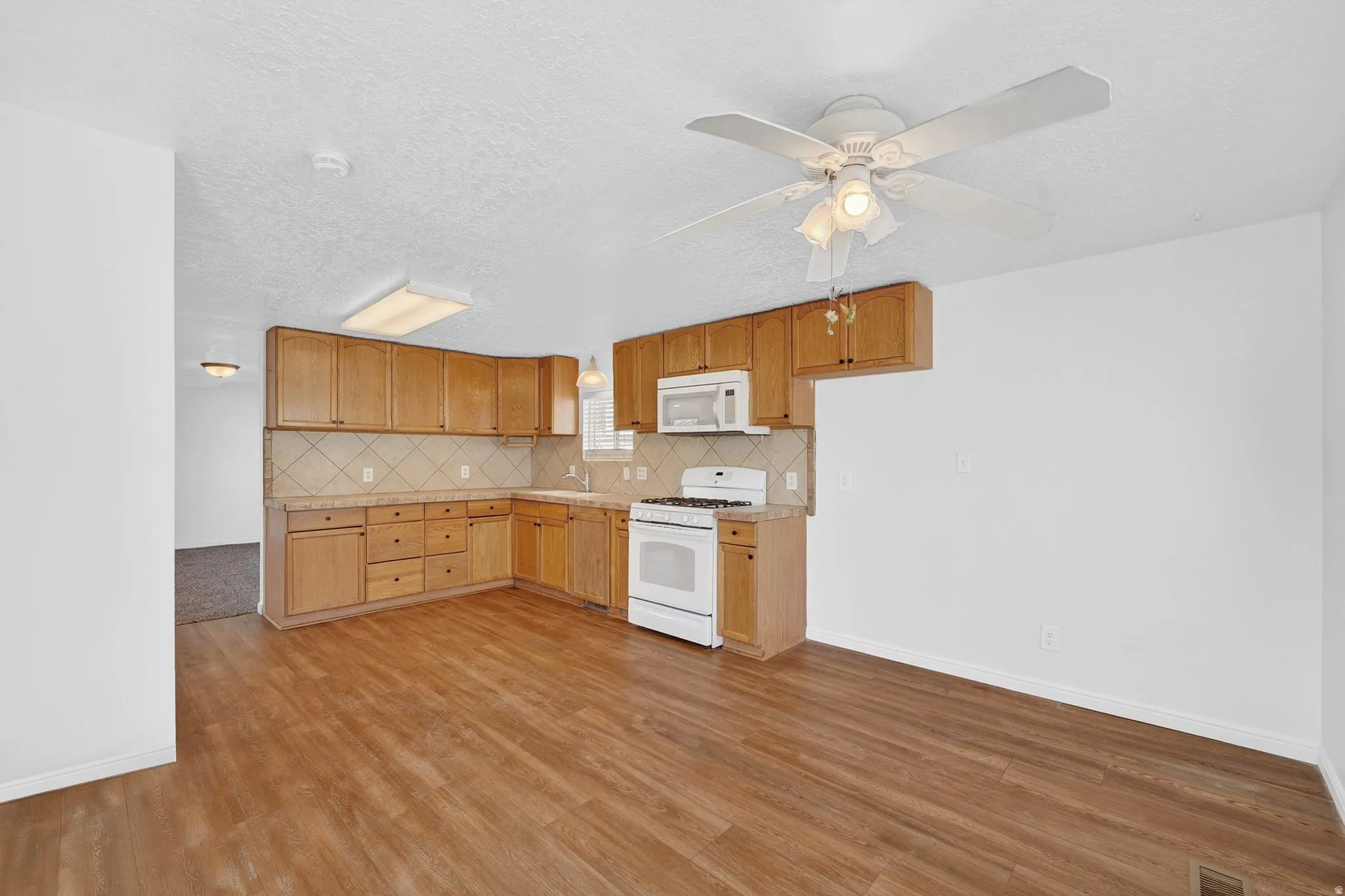 Kitchen featuring white appliances, ceiling fan, light countertops, backsplash, and light wood-style floors