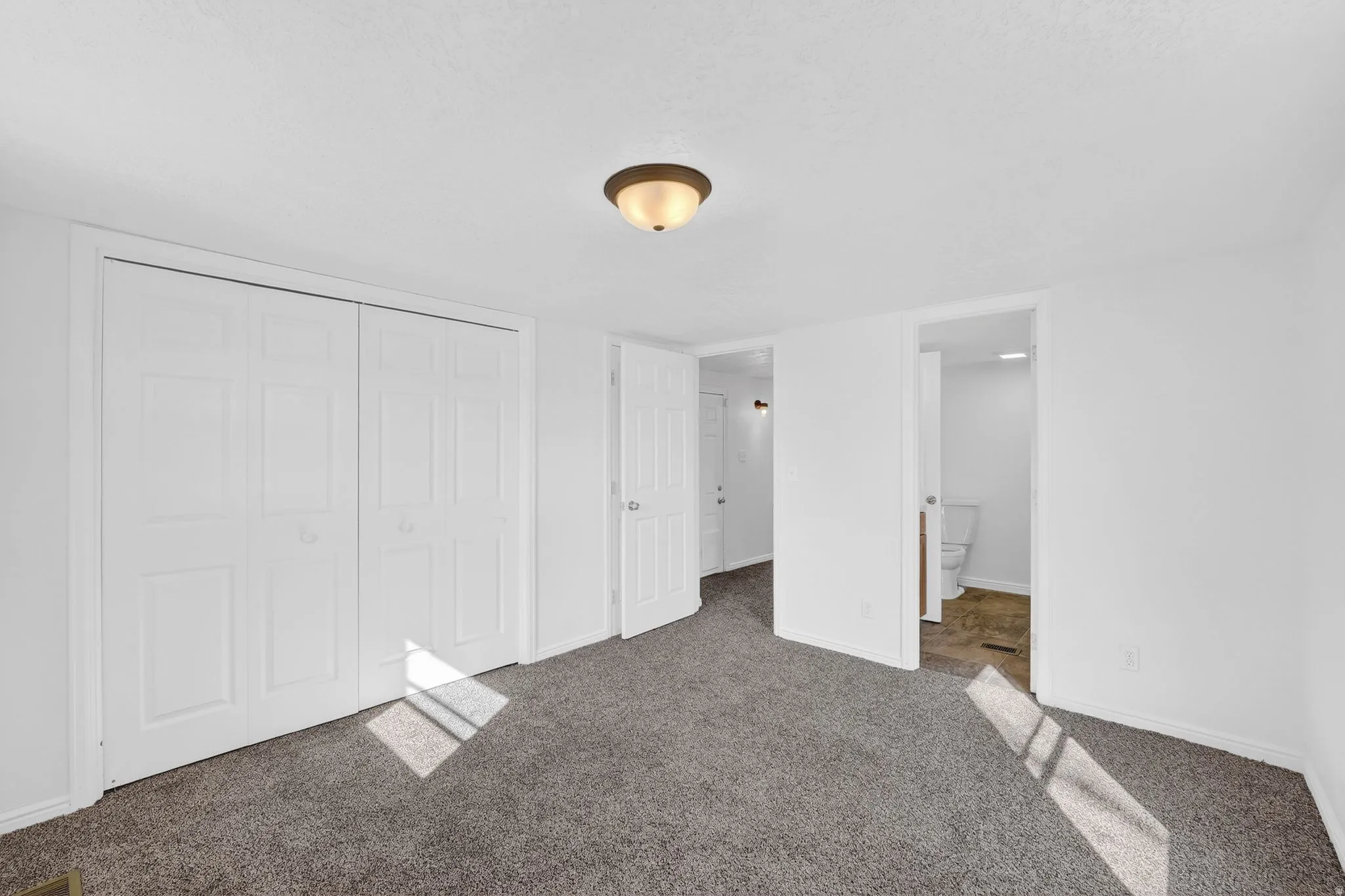 Unfurnished bedroom with ensuite bathroom, a closet, and carpet floors