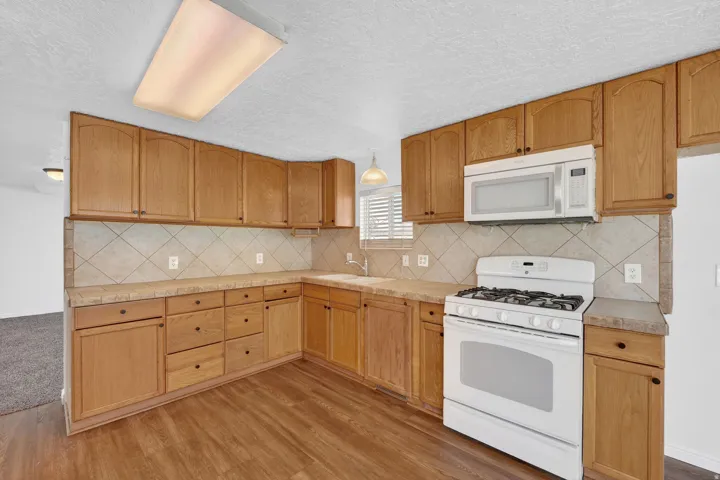 Kitchen featuring white appliances, light countertops, a textured ceiling, light wood finished floors, and decorative backsplash