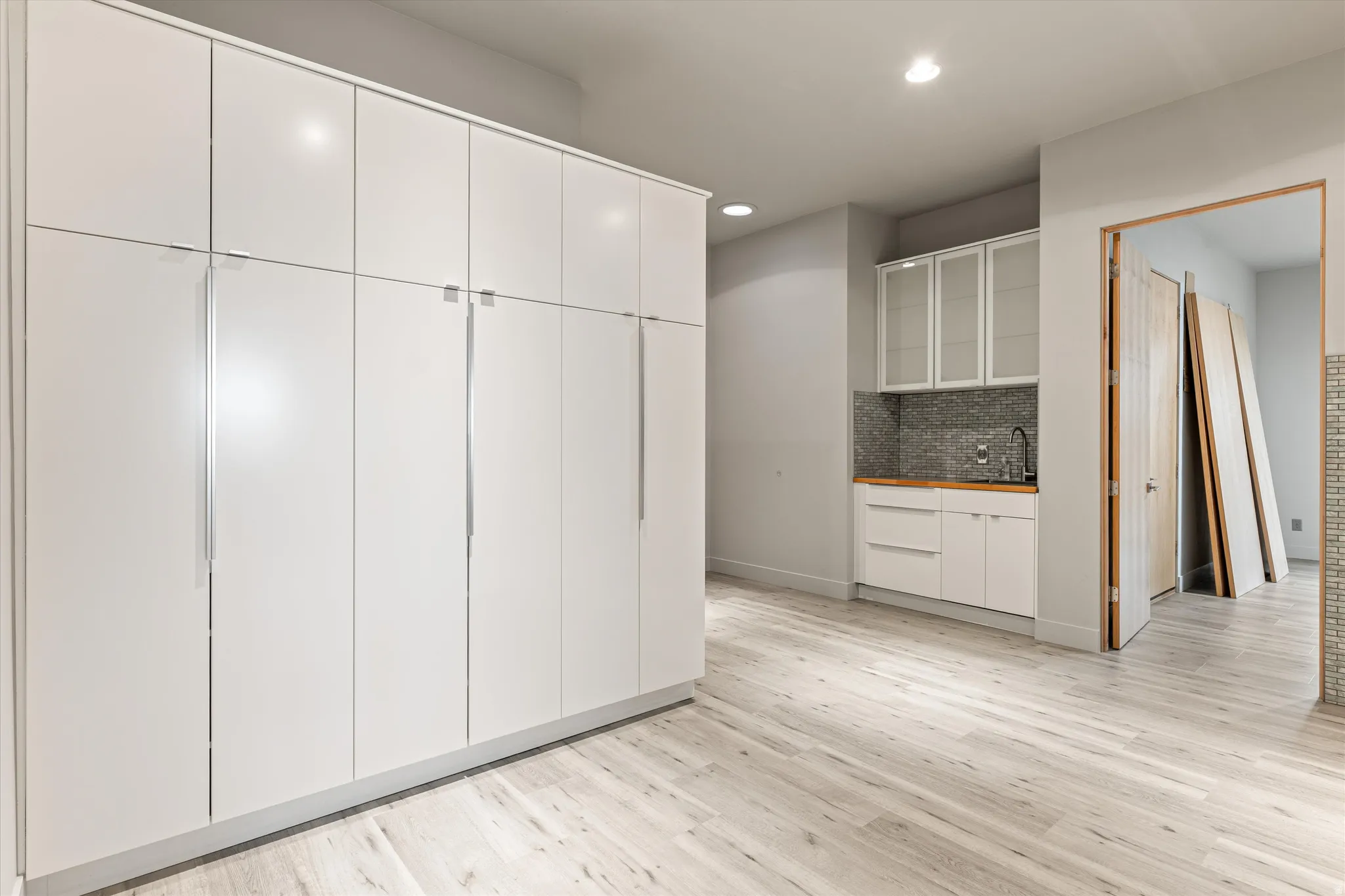 Kitchen with white cabinets, glass fronted cabinets, light wood-style flooring, tasteful backsplash, and recessed lighting