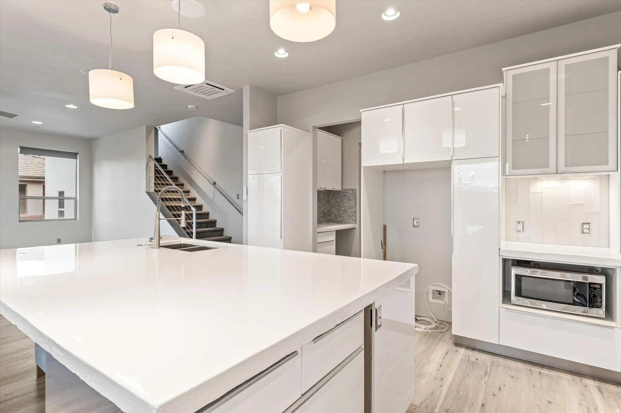 Kitchen with white cabinets, modern cabinets, pendant lighting, tasteful backsplash, and light wood finished floors