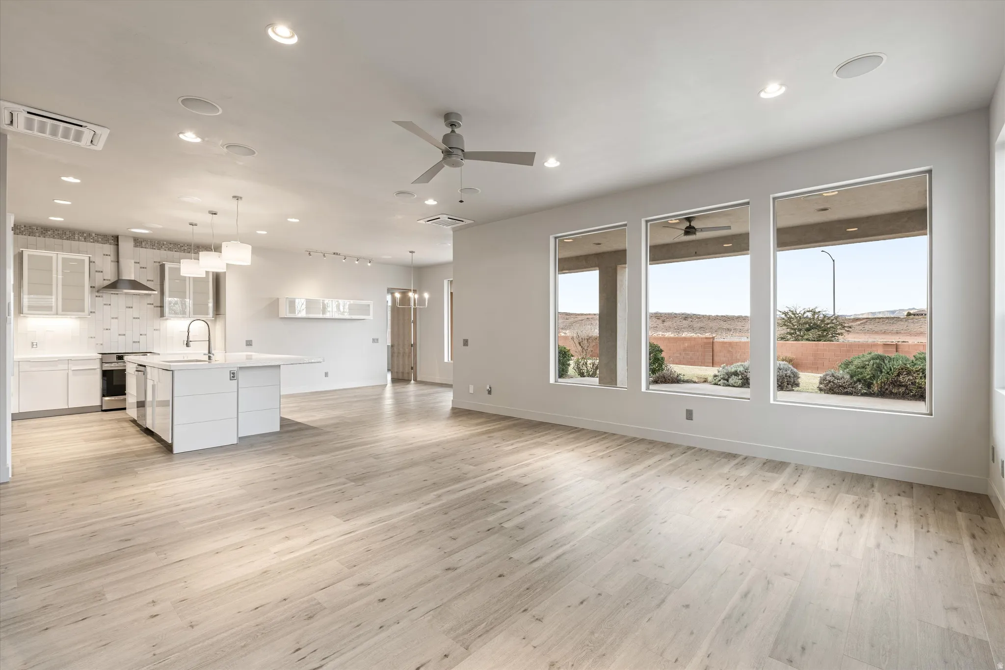 Unfurnished living room featuring light wood-type flooring, ceiling fan, and hanging lights