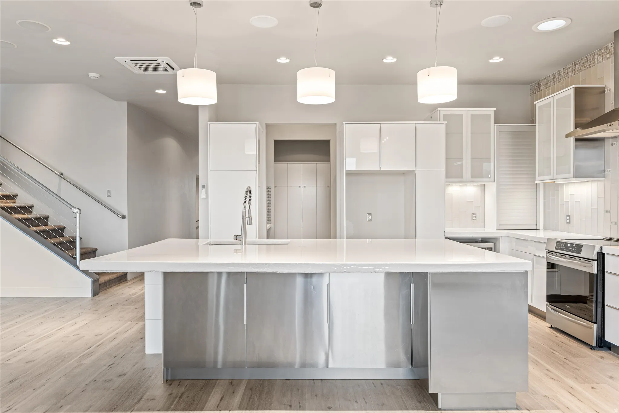 Kitchen with glass fronted cabinets, light wood-style floors, stainless steel electric range oven, pendant lighting, and a center island with sink
