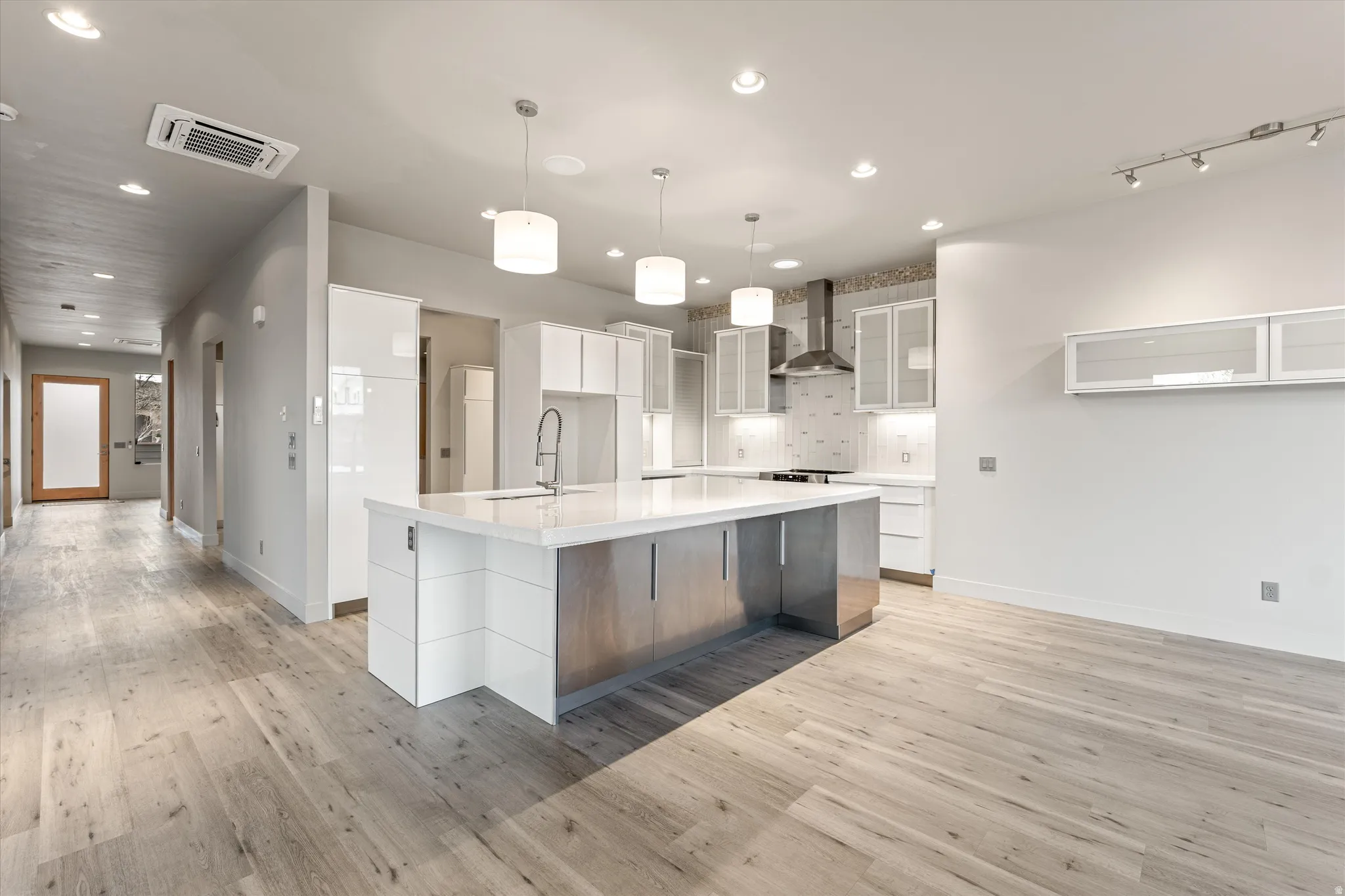 Kitchen with modern cabinets, a spacious island, glass insert cabinets, pendant lighting, and light wood finished floors