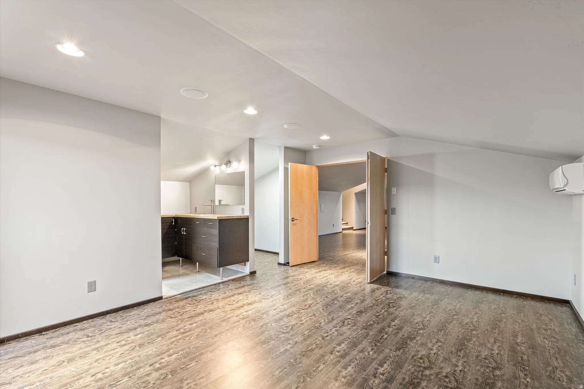 Unfurnished living room with wood finished floors, vaulted ceiling, and recessed lighting