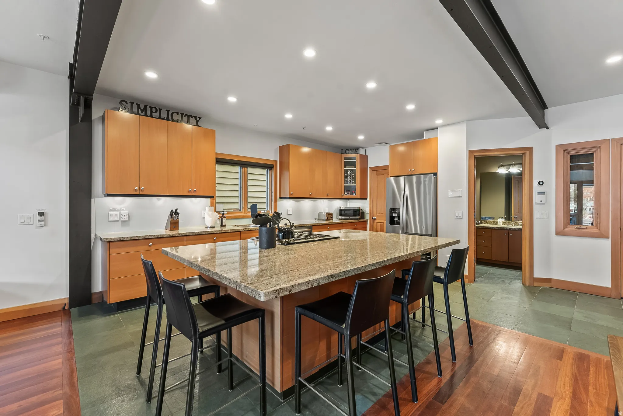 Kitchen with a breakfast bar area, beam ceiling, light stone counters, stainless steel fridge with ice dispenser, and a center island