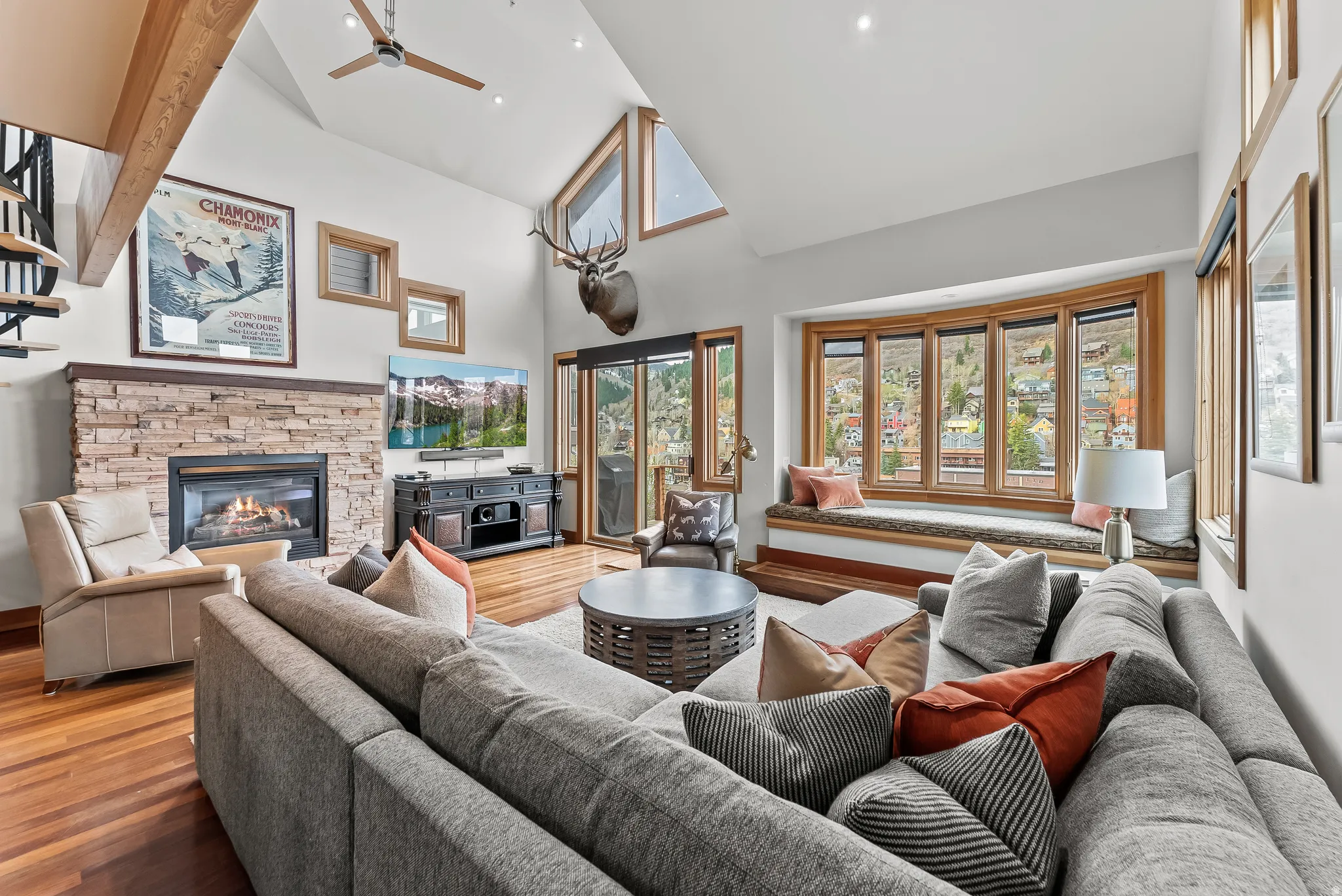 Living area featuring a stone fireplace, wood finished floors, a ceiling fan, and vaulted ceiling