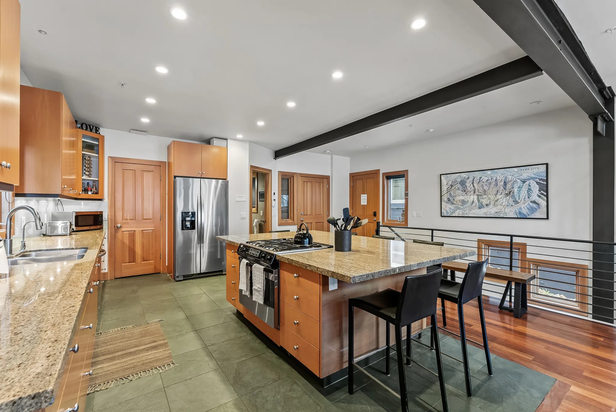 Kitchen featuring light stone counters, stainless steel appliances, glass insert cabinets, recessed lighting, and a kitchen bar