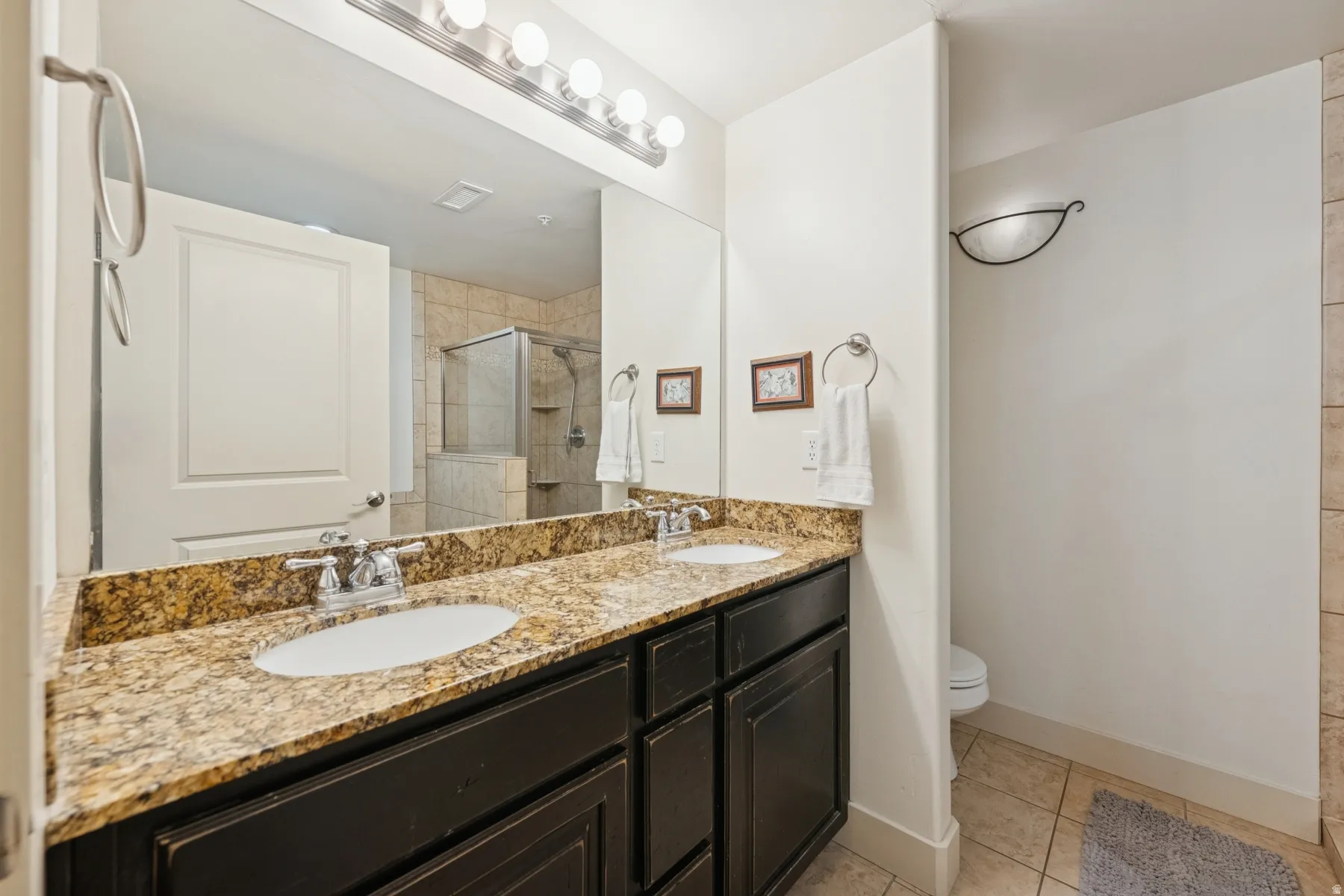 Full bath with double vanity, a shower stall, and light tile patterned floors