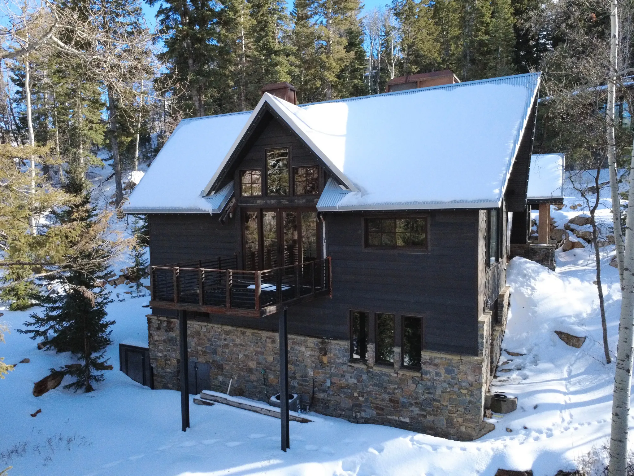 View of front of home featuring a chimney, stone siding, and view of wooded area