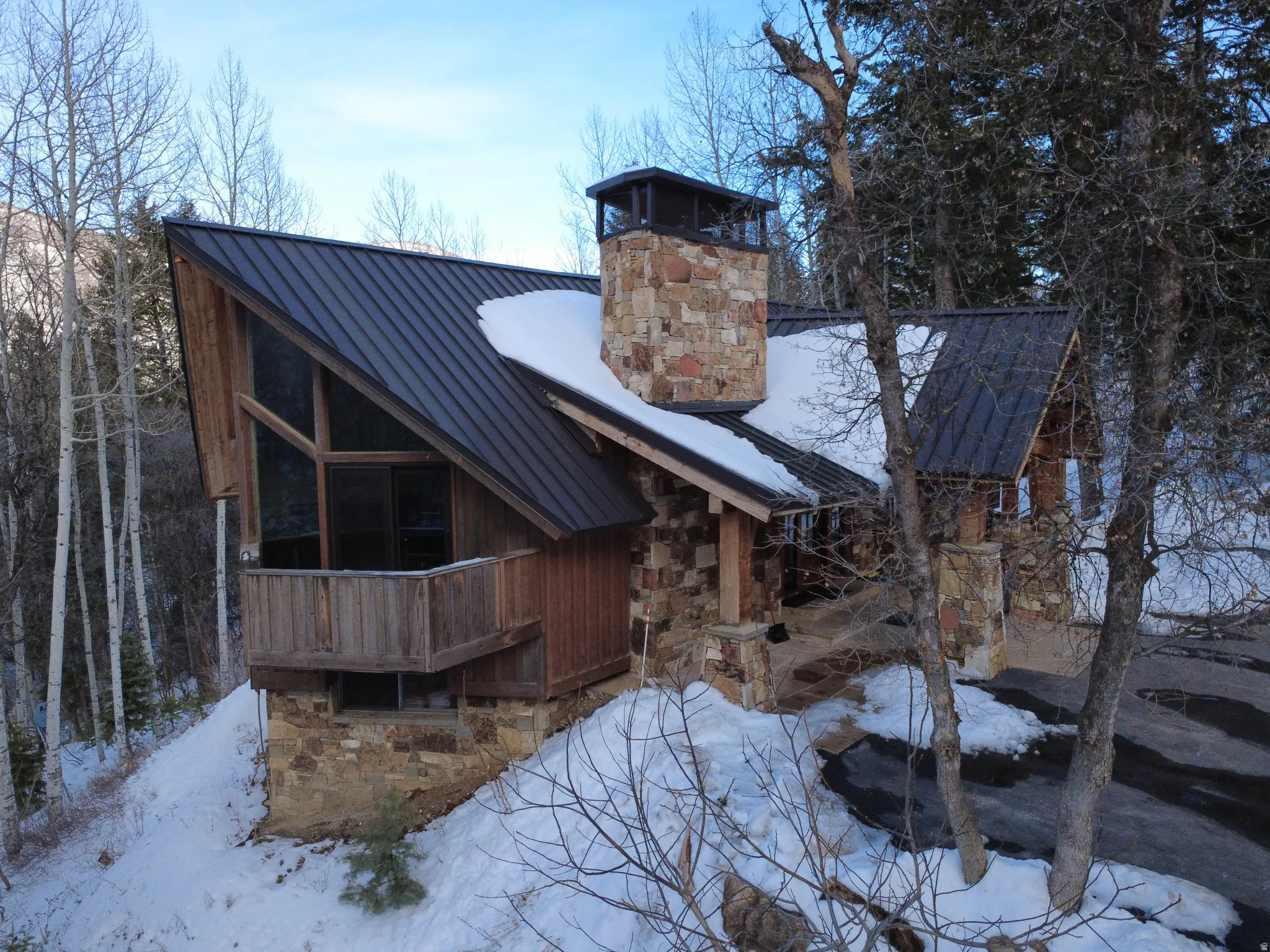 Snow covered property with stone siding, a standing seam roof, and a chimney
