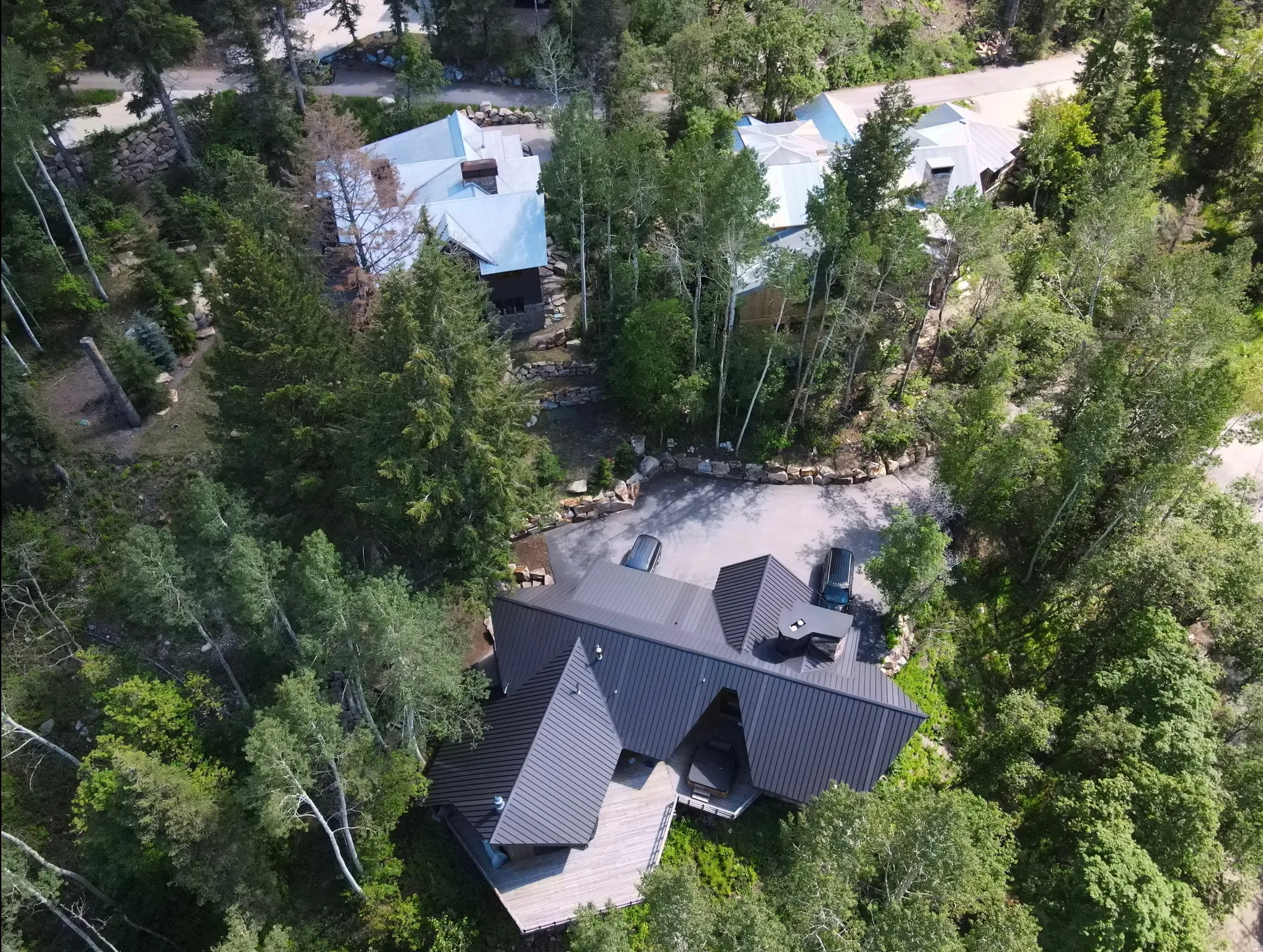 Modern sloped-roof architecture featuring a dark metal roof, expansive wood decking, and a stone-paved driveway