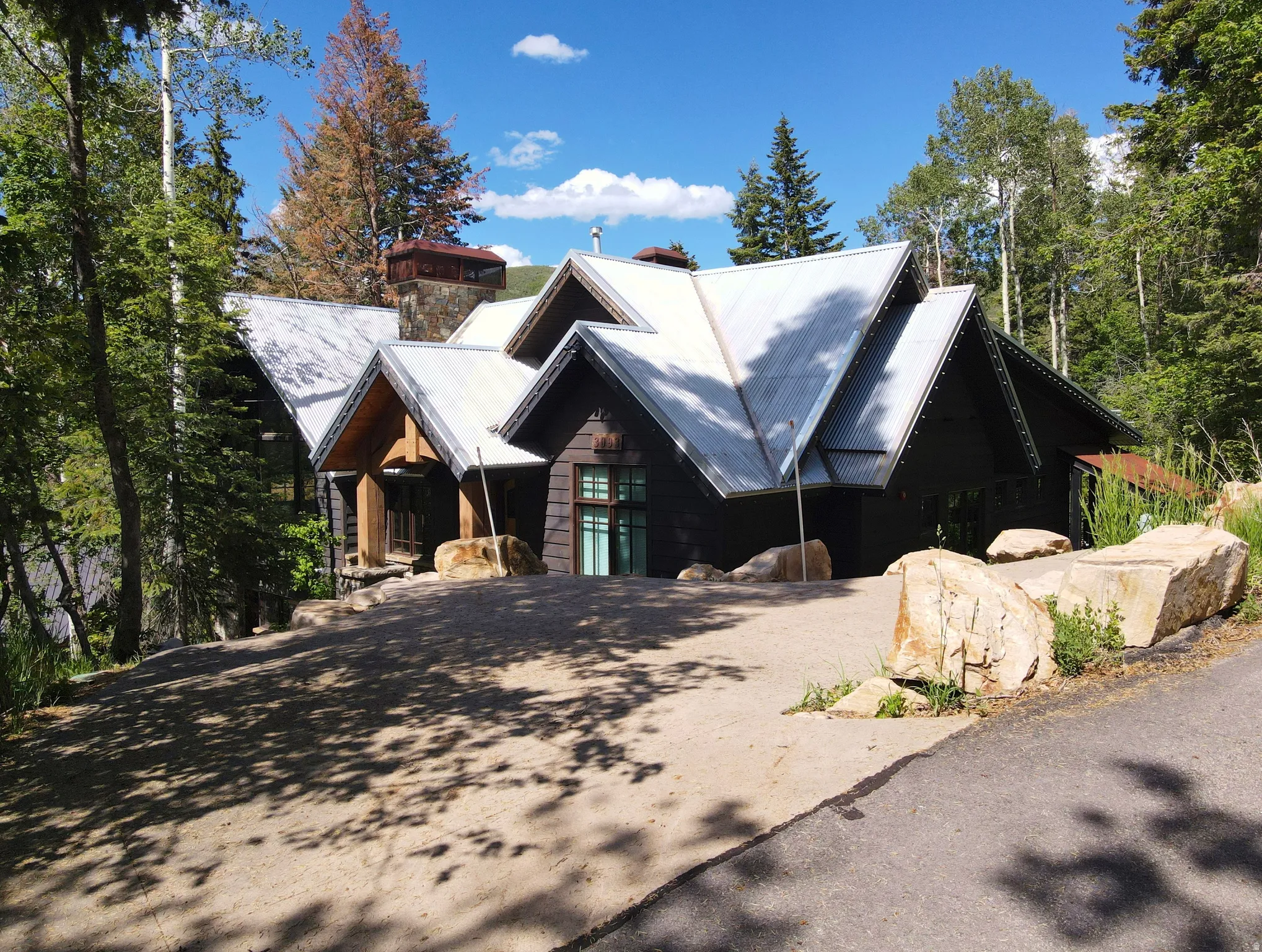 Architectural residence featuring a dark wood facade, multiple gabled roofs with metal covering, and a prominent stone chimney