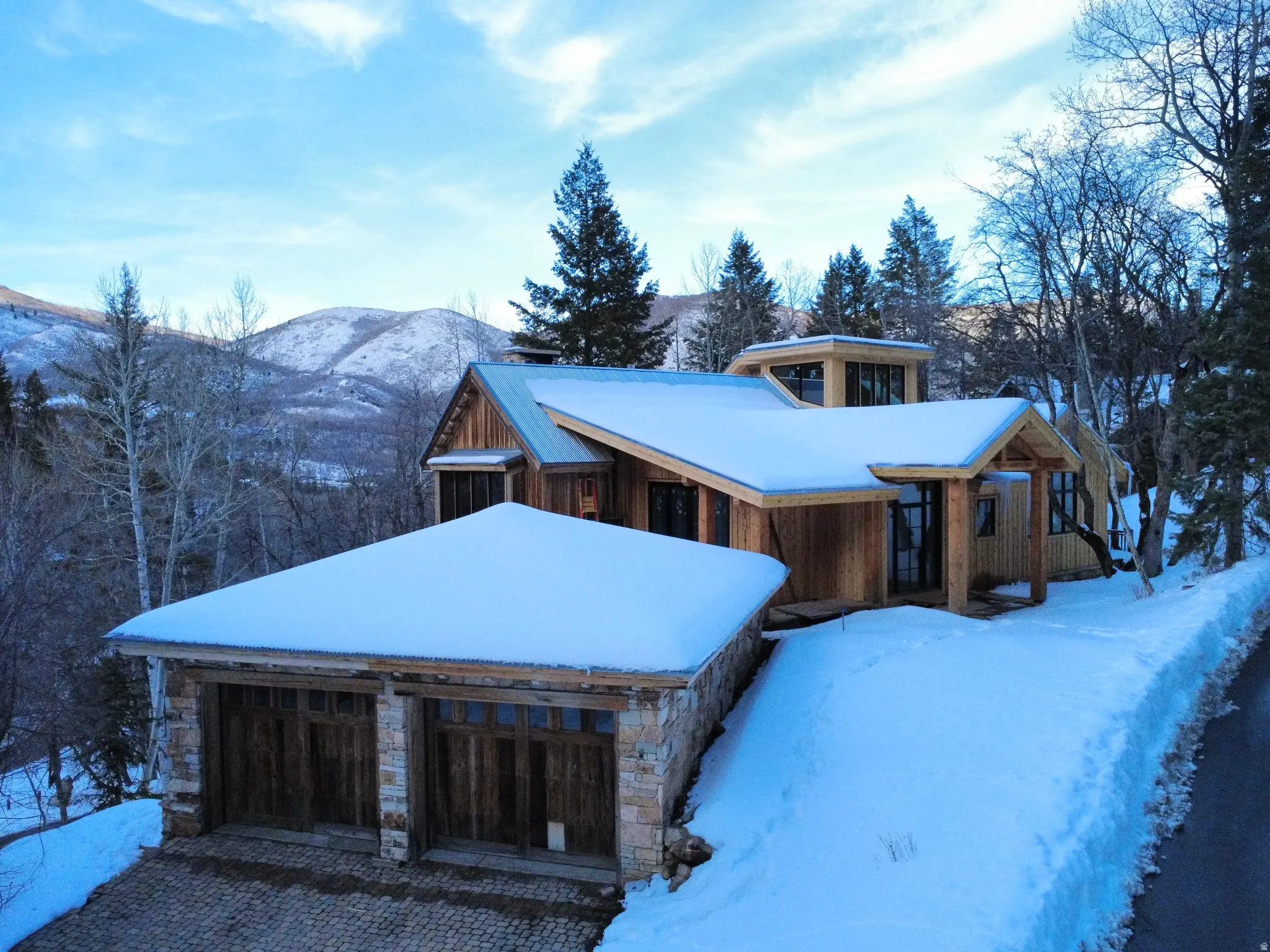 View of front facade featuring a mountain view, stone siding, a garage, and driveway