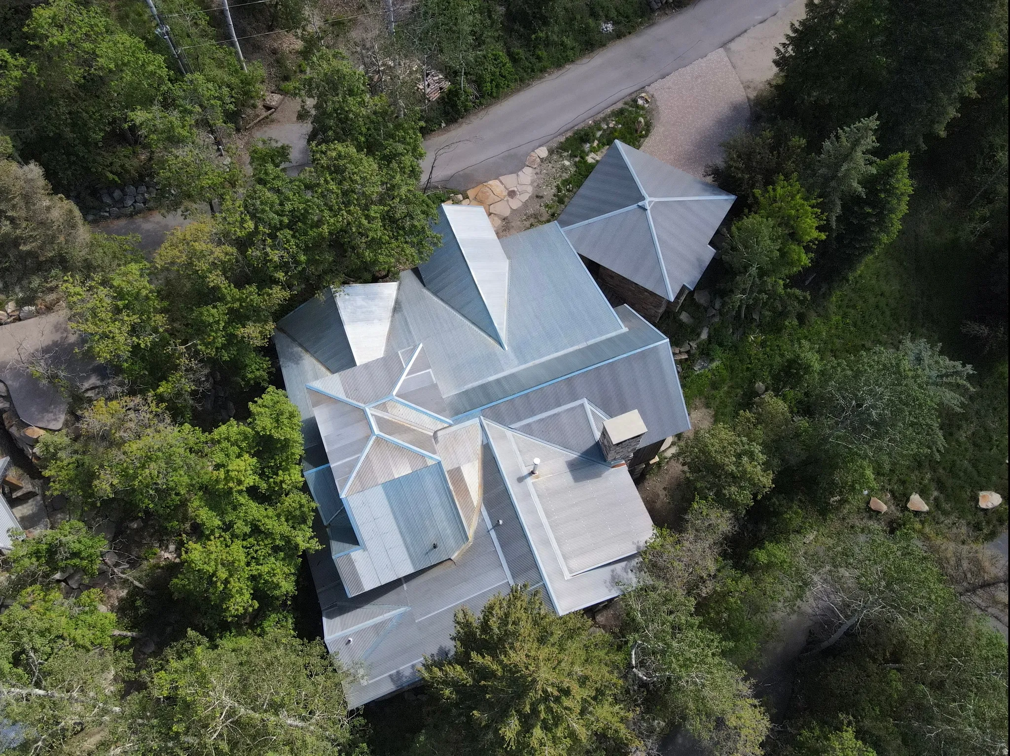 Property featuring a multi-faceted metal roof, integrated chimney, and a gravel driveway