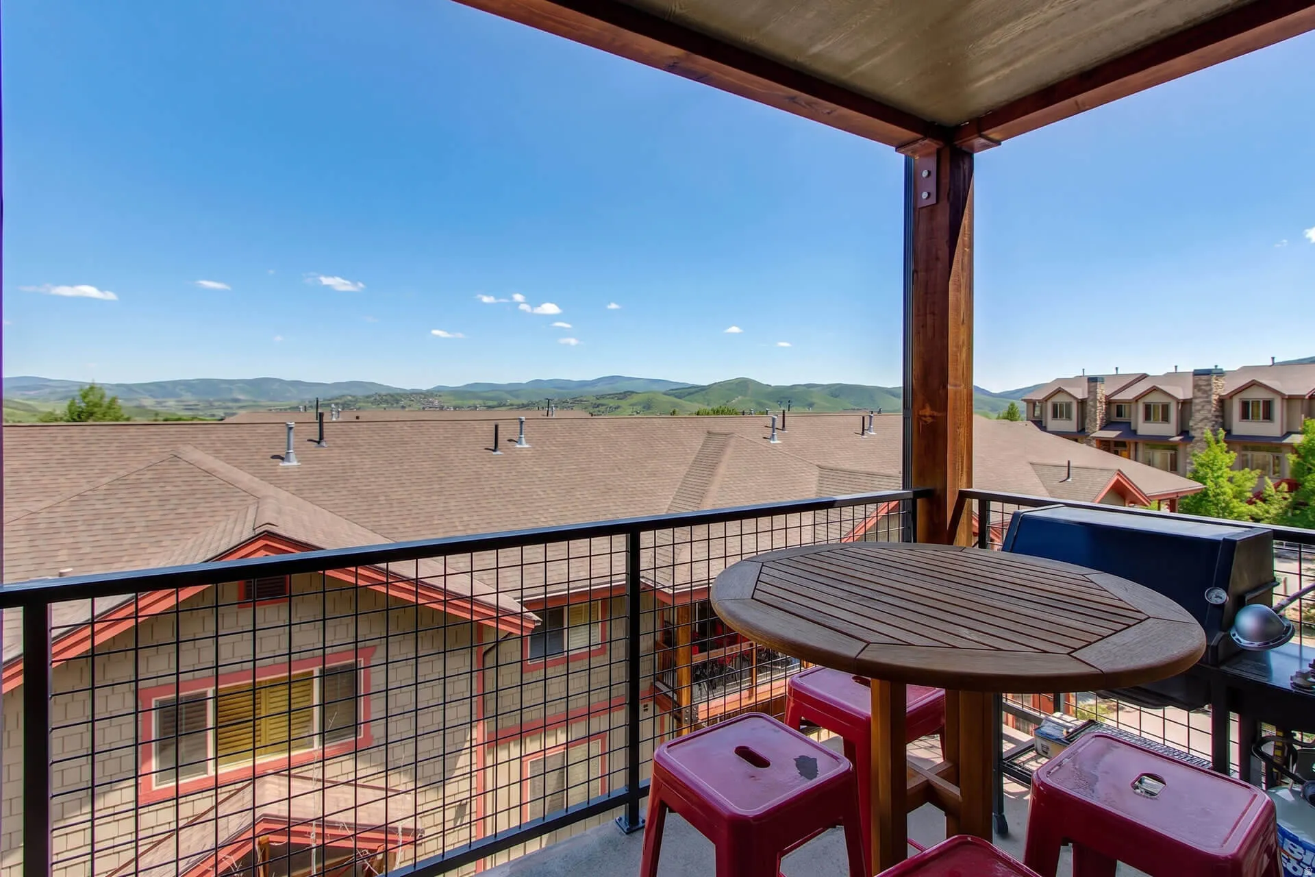 Private balcony with metal grid railing and wood-tone structural columns, offering expansive mountain scenery