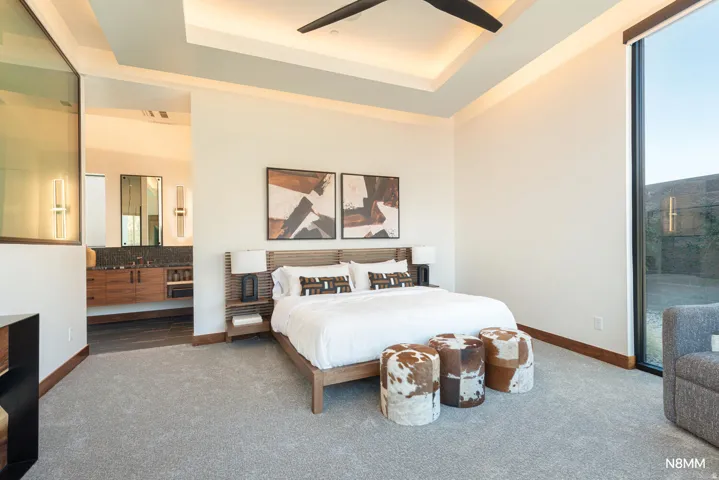 Carpeted bedroom with a ceiling fan, a raised ceiling, access to outside, and ensuite bathroom