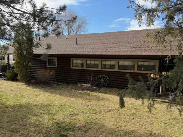 Rear view of property featuring a shingled roof, a yard, and log veneer siding