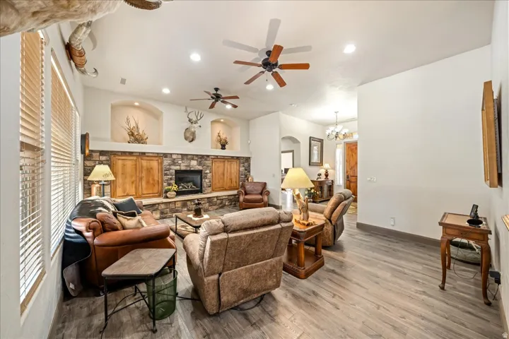 Living room with light wood-type flooring, a ceiling fan, hanging lights, a stone fireplace, and arched walkways